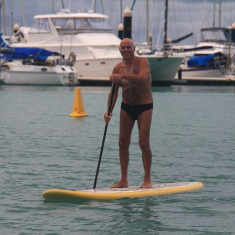 An old man in a spedo on a stand up paddle board